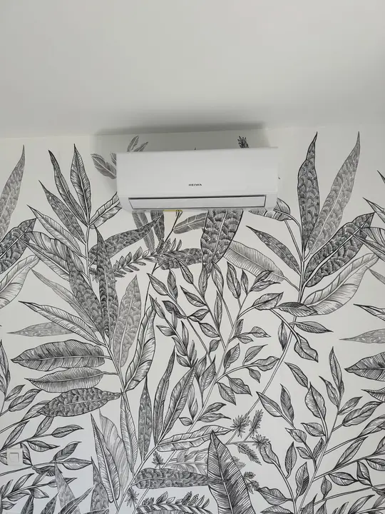 Split de climatisation posé sur un mur à papier peint végétal